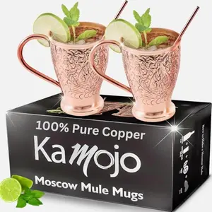 Two intricately embossed copper mugs with copper straws on a linen cloth