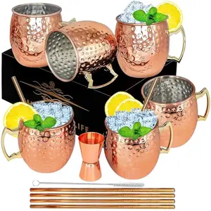 Set of six hammered copper mugs with straws and jigger on a wooden table