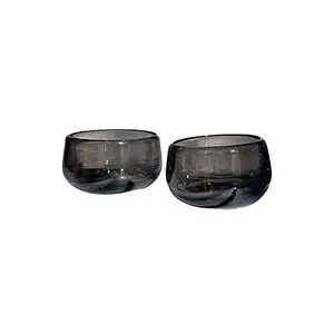 Two hand-blown mezcal glasses in smoke color on a wooden surface