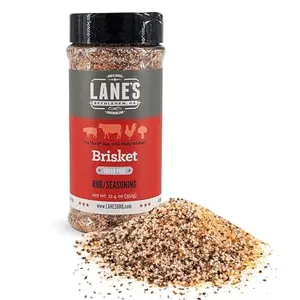 Lane's Brisket Rub seasoning bottle on a wooden table with grilled beef