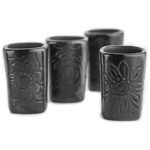 Four black clay mezcal glasses with square shape on a colorful Mexican tablecloth