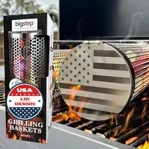 Two stainless steel round grill baskets with USA flag engraving on lids and accessories on a table