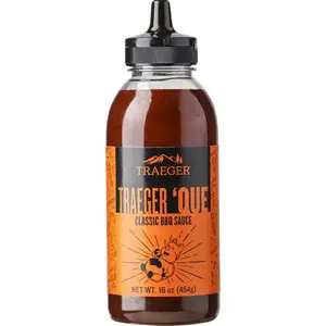 Traeger 'Que BBQ Sauce bottle on a wooden table next to grilled chicken