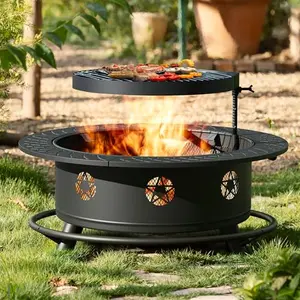 Round black metal fire pit with grill, lid, and poker in a garden setting