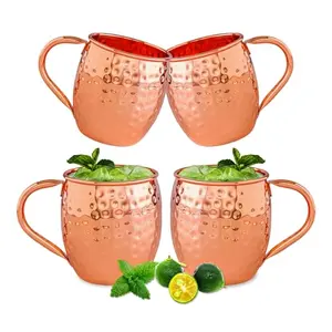 Four solid copper mugs with classic barrel shape displayed on a rustic wood table
